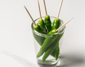 Verscheidenheid aan verse groene chilipepers, op een spies gestoken en rechtopstaand, met een glanzende, gladde textuur en een levendige groene kleur, bedoeld als condiment of garnering voor een pittig gerecht.