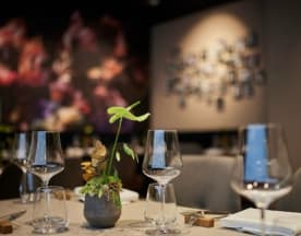 Modernes Restaurantinterieur mit eleganter und schlichter Gestaltung, klaren Gläsern und einem minimalistischen Pflanzenarrangement als Mittelpunkt, ergänzt durch eine sanft beleuchtete Fotowand.