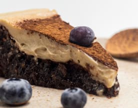 Uma fatia de bolo de chocolate rico, com uma textura densa e húmida, coberta com um creme suave e brilhante, polvilhada com cacau e acompanhada de mirtilos frescos.
