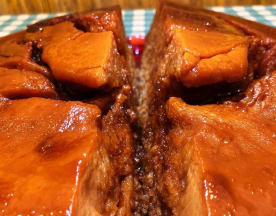 Um grande pedaço de carne, provavelmente de porco, apresentado em um molho escuro e rico, com uma textura tenra e suculenta, coberto por uma camada de gordura. O molho espesso e caramelizado sugere um sabor doce e salgado, com o interior bem cozido e infundido com o molho.