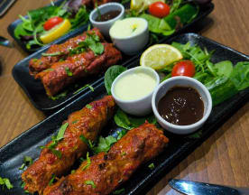 Chargrilled kebabs garnished with fresh herbs, served with creamy and savory dipping sauces, alongside a mix of greens, cherry tomatoes, and lemon wedges.