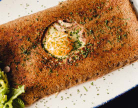Galette de sarrasin dorée et croustillante, garnie d'un œuf coulant et de tranches de jambon, accompagnée d'une salade verte croquante et de radis.