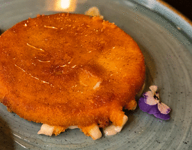 Fritura de queso dorada y crujiente, acompañada de mermelada de frutas rojas y flores comestibles.