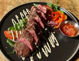 Perfect gebakken steak, gesneden in malse stukken, geserveerd op een bed van verse groenten, gegarneerd met dunne schijfjes tomaat en kleurrijke paprika's, met een scheutje romige saus en een bijgerecht van verse tomatensalsa.