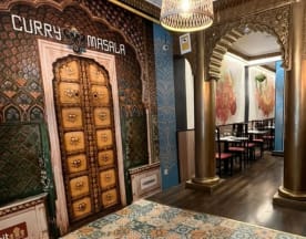 El interior del restaurante presenta un ambiente cálido y acogedor, con una decoración rica y ornamentada, incluyendo un mural de una puerta intrincadamente diseñada y obras de arte coloridas que reflejan la herencia culinaria.