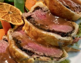 Fatias de beef Wellington com carne tenra envolta em massa folhada dourada, acompanhadas por duxelles de cogumelos e um molho marrom rico, servidas com uma mistura colorida de legumes assados.