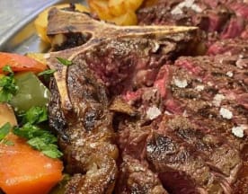 Tomahawk a la parrilla, jugoso y tierno, con costra caramelizada y acompañado de papas asadas y verduras salteadas.