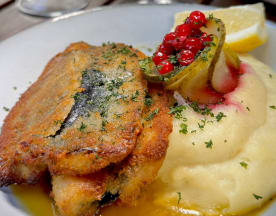 Två gyllenbruna friterade fiskfiléer, krispiga på utsidan och möra inuti, garnerade med färska örter. Serveras med krämig potatismos och toppad med inlagd jalapeño och röda bär, samt en citronskiva vid sidan.