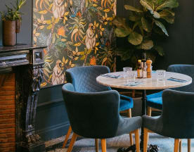 Intérieur de restaurant chaleureux avec une table en marbre entourée de chaises rembourrées bleu profond, décoré d'une fresque florale et d'une grande plante en pot.