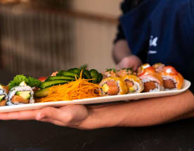 Prato de sushi bem apresentado, com uma variedade de rolls, incluindo salmão e camarão frescos, além de recheios de pepino e abacate, decorado com cenoura e ervas.