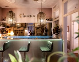 Área de bar elegante com balcão iluminado, bancos estofados em tecido verde e iluminação quente de pendentes ornamentais, criando uma atmosfera acolhedora.