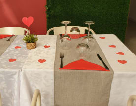 Mesa elegantemente decorada para uma ocasião romântica, com toalhas brancas e cinzentas, corações de papel vermelhos e guardanapos vermelhos dobrados, criando uma atmosfera acolhedora.