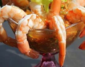 Prato de marisco refrescante com camarões suculentos dispostos em volta de uma taça, acompanhados de um molho de cocktail picante à base de tomate e especiarias, guarnecido com aipo.
