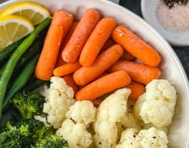 Uma colorida seleção de legumes frescos, incluindo cenouras baby laranja, feijão verde crocante e floretes de couve-flor tenros, com uma porção generosa de brócolos e gomos de limão para um contraste cítrico.