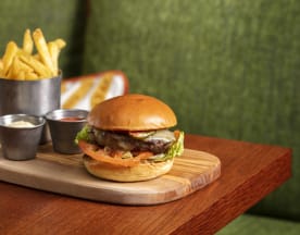 Juicy hamburger with a grilled beef patty, fresh lettuce, tomato, and melted cheese in a soft bun, served with crispy French fries and two dipping sauces.