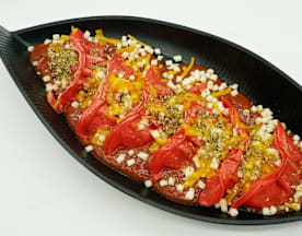 Pimientos rojos sobre una salsa sabrosa, con queso derretido y hierbas, decorados con tiras de pimientos amarillos.