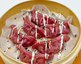 Dumplings delicados de color rosa, con salsa cremosa y semillas de sésamo negro, presentados en una vaporera de bambú.