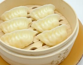 Seis delicados dumplings al vapor con un exterior suave y brillante, rellenos de carne picada y verduras.