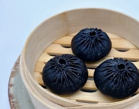 Tres baos negros, suaves y esponjosos, elaborados con carbón activado o tinta de calamar, presentados en una vaporera de bambú.