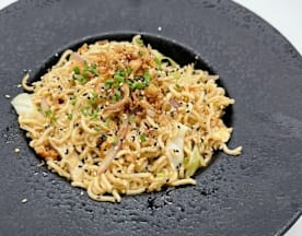 Fideos salteados con cebolla frita crujiente, cebollín picado y semillas de sésamo negro, acompañados de repollo.