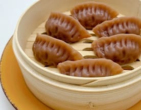 Seis dumplings rellenos, con un exterior marrón brillante y textura arrugada, presentados en una vaporera de bambú.