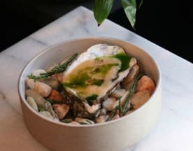 A large oyster with a light, creamy hue, drizzled with green herb sauce, garnished with asparagus spears and presented on pebbles and seaweed.
