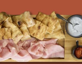 Selezione di focacce dorate e salumi, accompagnati da una salsa cremosa e una salsa rossa piccante.