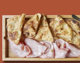 Selezione di focacce dorate e affettati, accompagnati da una salsa cremosa e un condimento rosso, ideale per uno spuntino conviviale.