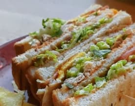 Gelaagde sandwich van zacht witbrood, gevuld met gescheurde sla, tomaat en een eiwit, mogelijk kip of kalkoen, geserveerd met schijfjes citroen.