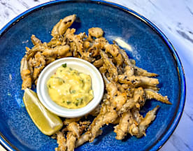 Plat de poisson frit croustillant, garni d'herbes fraîches, accompagné d'un bol de sauce crémeuse et d'un quartier de citron vert.
