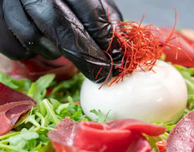 Burrata cremosa su un letto di rucola fresca, con fette di prosciutto e fili di zafferano.