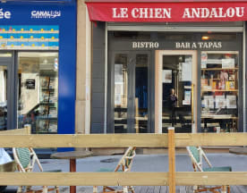 Extérieur du bistro "Le Chien Andalou" avec un auvent rouge, des portes en verre et des tables avec chaises rayées vertes et blanches, créant une ambiance décontractée pour déguster des tapas et des boissons.