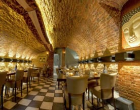 Het interieur van het restaurant heeft een unieke, gebogen bakstenen plafond en elegante, gevoerde stoelen rond lange houten tafels, wat bijdraagt aan een warme en uitnodigende sfeer.
