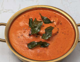 Creamy tomato-based curry garnished with fresh curry leaves and black mustard seeds, offering a rich flavor and smooth texture.