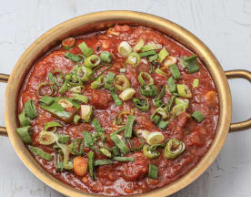 Hearty tomato-based sauce with vegetables, topped with sliced green onions for a fresh crunch.
