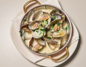 Mexilhões cozidos no vapor, servidos nas suas conchas e mergulhados num caldo cremoso com alho e ervas, guarnecidos com ervas verdes picadas.