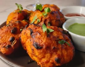 Fritters crocantes de batata temperada, guarnecidos com ervas frescas e acompanhados de molhos de mergulho vermelho e verde.