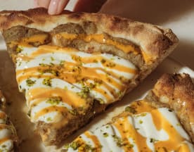 Pizza con crosta spessa e dorata, con salsa bianca cremosa e un tocco di salsa arancione piccante, guarnita con erbe fresche tritate.