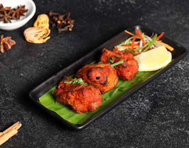 A trio of golden-brown lentil or chickpea fritters garnished with fresh herbs, served with a wedge of lemon and a side of finely sliced crunchy vegetables.