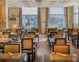 Interior moderno y espacioso con grandes ventanales, mesas ordenadas y sillas de colores claros, creando un ambiente acogedor y elegante.