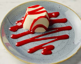 Romige panna cotta, gegarneerd met een heldere frambozensaus die een zoete en pittige tegenhanger biedt, met een aantrekkelijke presentatie die het dessert licht en verfrissend maakt.