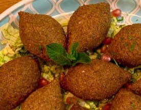Kibbeh dorada y crujiente, rellena de carne especiada y bulgur, acompañada de semillas de granada y salsa cremosa de yogur.
