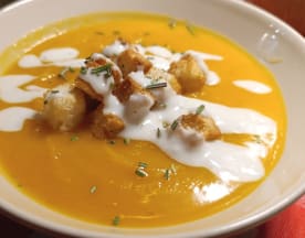 Sopa cremosa de abóbora, com um tom laranja rico, guarnecida com um fio de natas brancas, croutons dourados e ervas picadas.