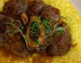 Prato rico com pedaços tenros de carne braçada, possivelmente vitela, sobre um risotto cremoso de açafrão, guarnecido com ramos de tomilho fresco.