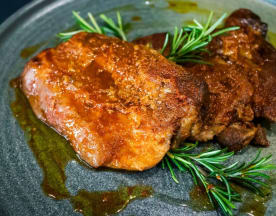 Carne di maiale arrosto con glassa caramellata, guarnita con rosmarino fresco e servita con una salsa saporita.