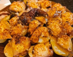 Pulpo a la parrilla sobre una cama de papas doradas, sazonado con especias que realzan su sabor.