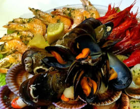 Plato de mariscos con mejillones, vieiras, camarones y langostinos, acompañado de rodajas de limón y servido sobre una cama de hojas verdes.