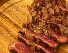 Bife grelhado, cortado em fatias grossas, com uma crosta perfeita e centro suculento, polvilhado com ervas secas.