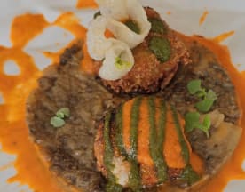 Croquetas doradas sobre puré de frijoles negros, con salsa naranja picante, salsa verde fresca y microgreens, acompañadas de elementos crujientes.