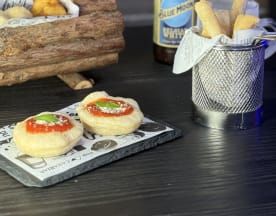 Aperitivos redondos con salsa roja y hierbas frescas sobre una base de pan suave, acompañados de papas fritas crujientes.